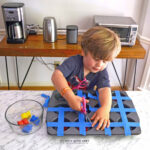 Toddler using scissors to cut back painter's tape from a muffin tin to find little plastic bears.