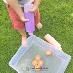 A preschooler squirting purple water into a water sensory bin filled with numbers.