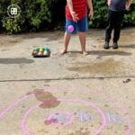 Child tossing a reusable water balloon on a target drawn with chalk.