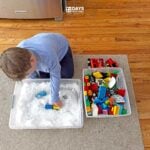 Young child playing with Duplos inside a sensory bin that is filled with snow.
