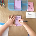 Child writing his name on a notebook for a class Valentine.