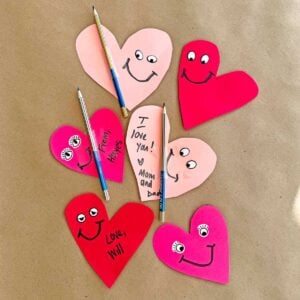 Collection of DIY heart Valentines with sticker eyes and smiles. The cards also have a rainbow pencil to gift for a class Valentine.