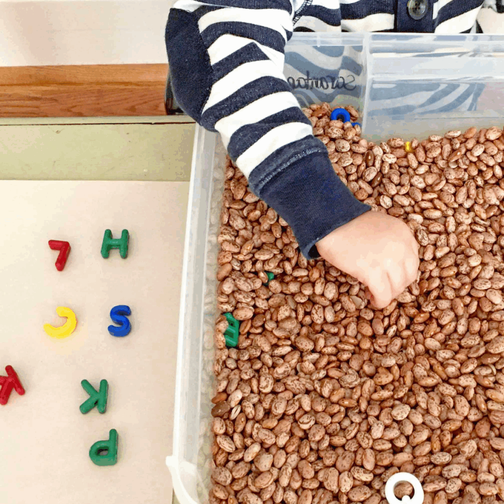 Toddler in a bean sensory bin pulling out different letters.