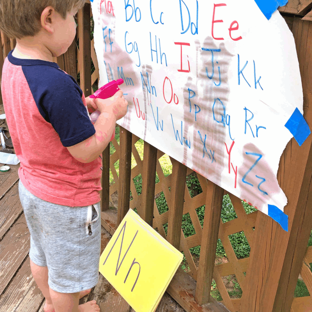 Child spraying letters written on paper with capital letters and lower case to match what alphabet card he pulled from the deck.