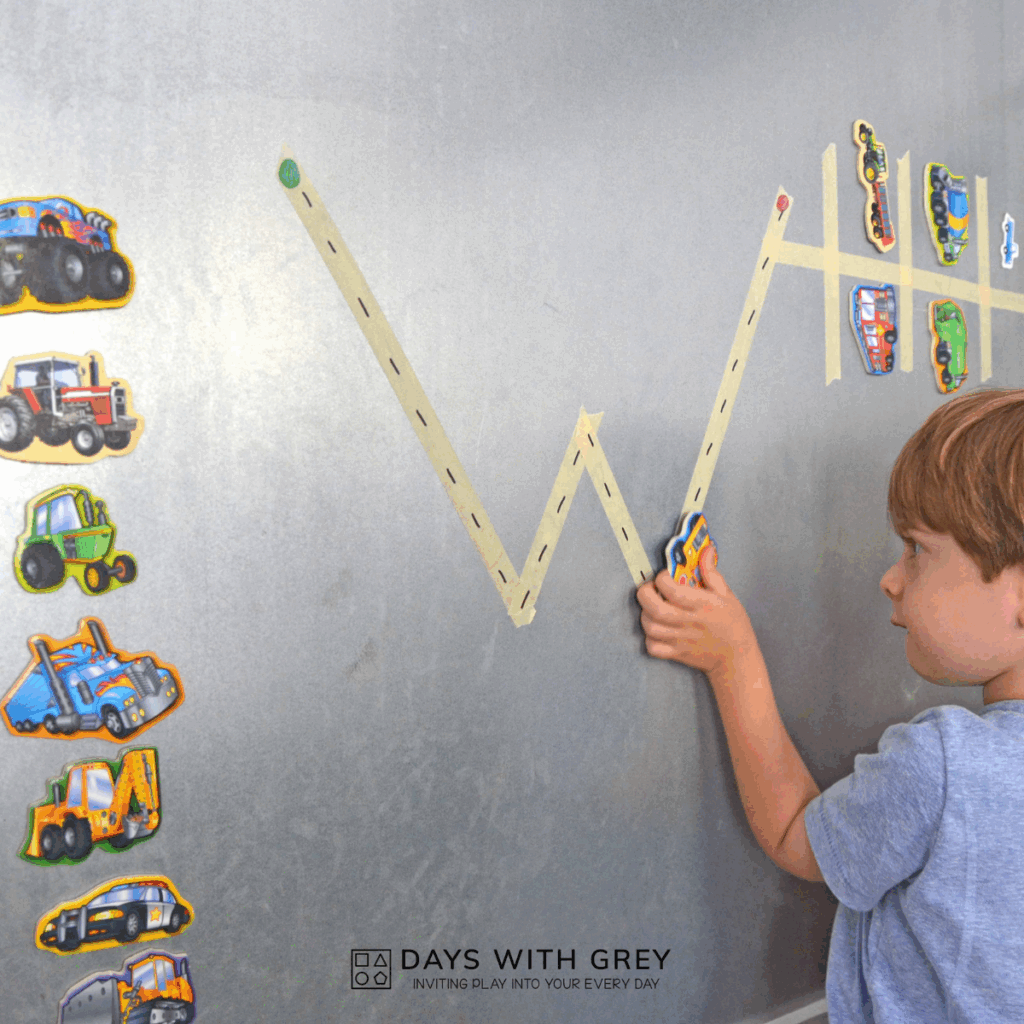 Child tracing the letter W with magnetic cars written with masking tape on a magnetic wall.