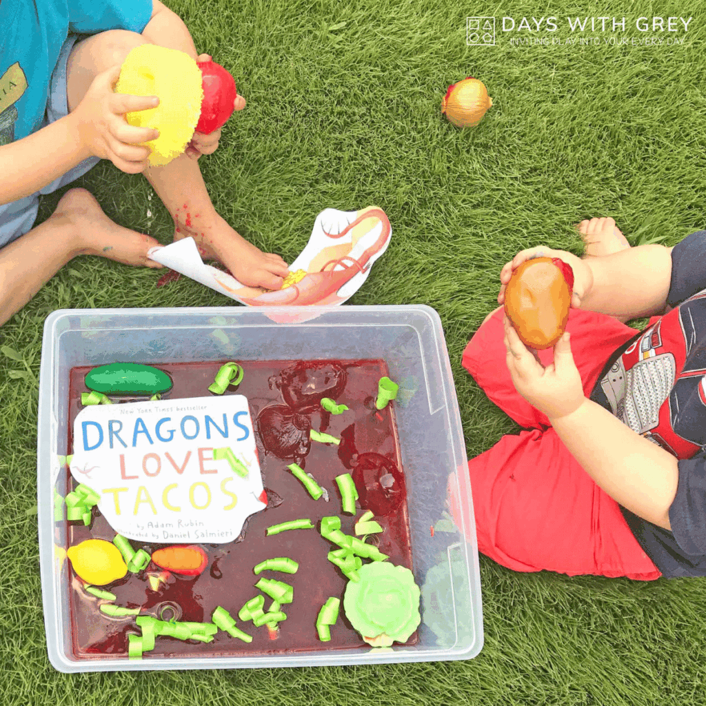 Jello sensory bin to retell the book Dragons Love Tacos. Two kids washing pretend food from a jello sensory bin.