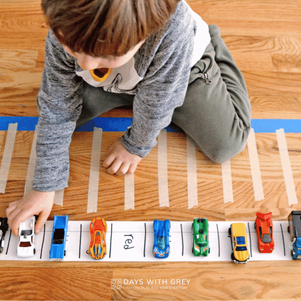A kindergartener sorting cars into the parking lot that has the color word on it.