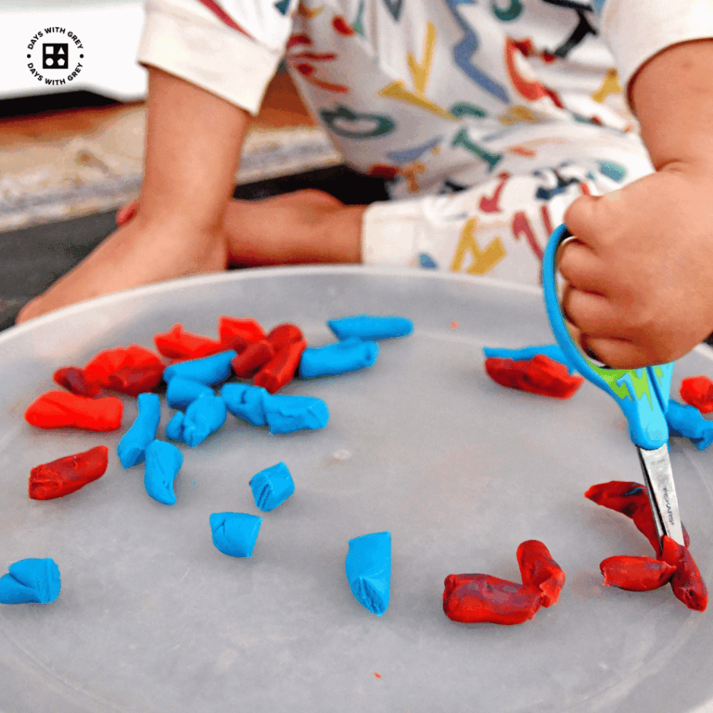 A young child cutting Play-Doh with scissors.