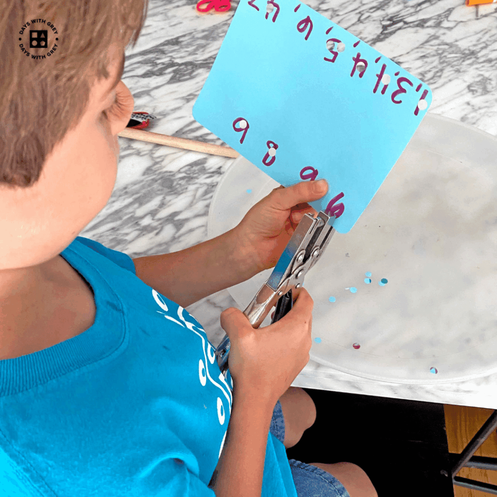 A kindergartener using a hole puncher to help strengthen his hands.