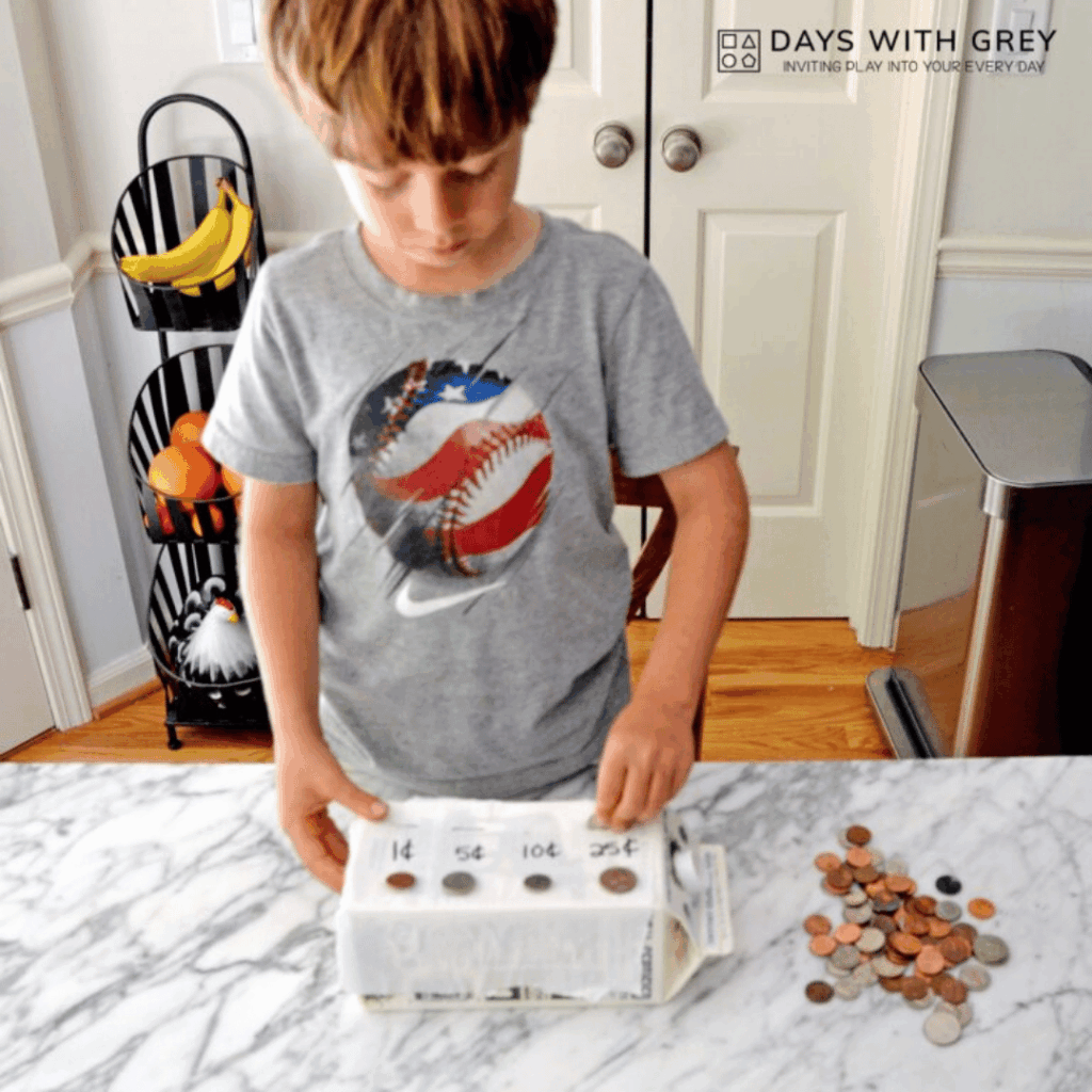 A five year old sorting coins into a homemade bank from a milk carton.