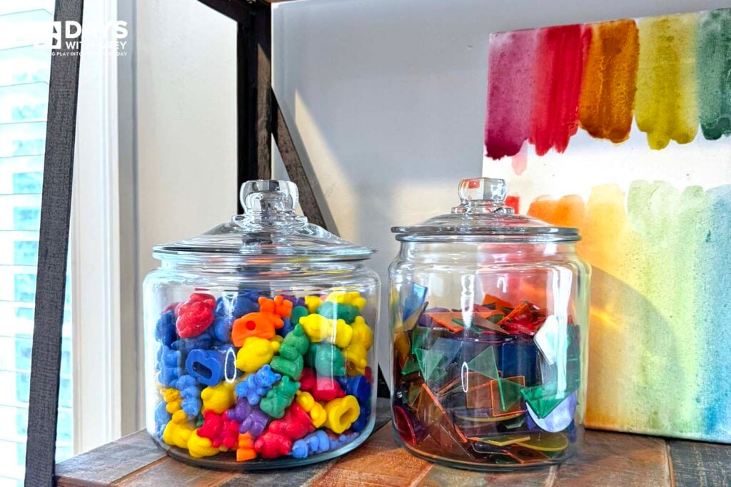 Counting bears and transparent shapes stored in glass containers on the shelf of a playroom.