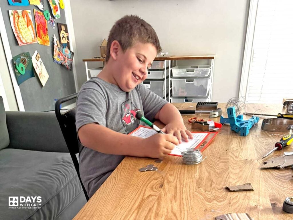 A young boy with a smile on his face as he checks off his list. The list is pretending to be a school schedule for kids to practice finding their classes at home.